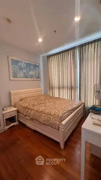 Cozy bedroom with wooden flooring and large window, featuring a comfortable bed and elegant decor.