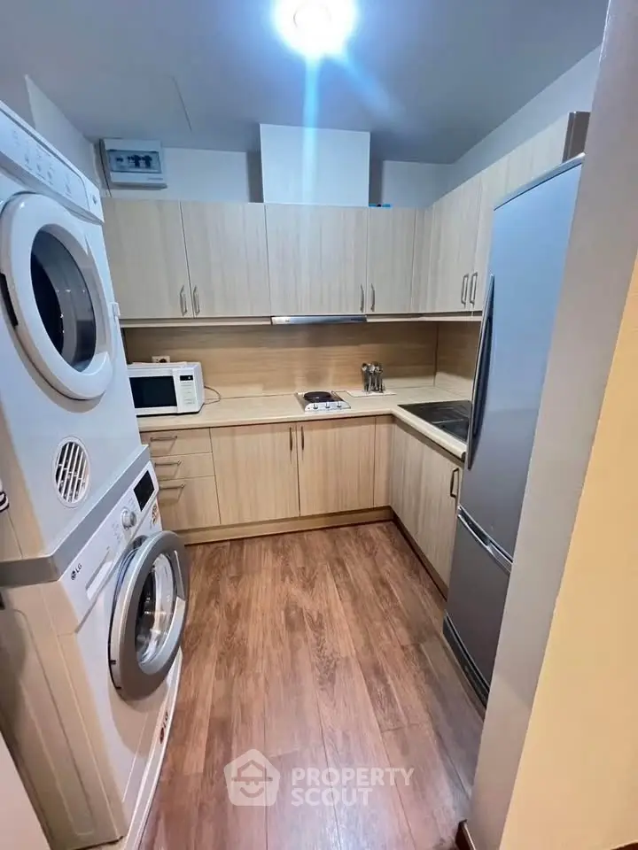 Modern kitchen with wooden cabinets, stacked washer-dryer, and sleek appliances in a compact layout.