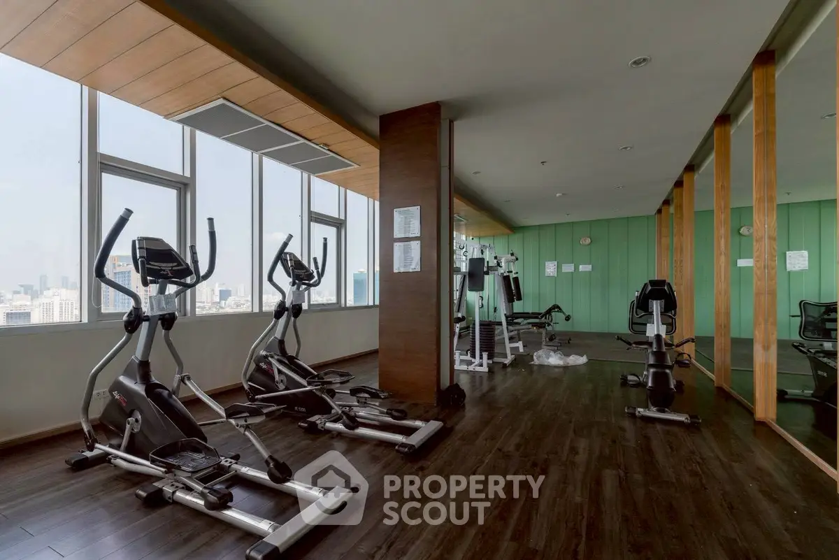 Spacious gym with modern equipment and city view in luxury apartment building.