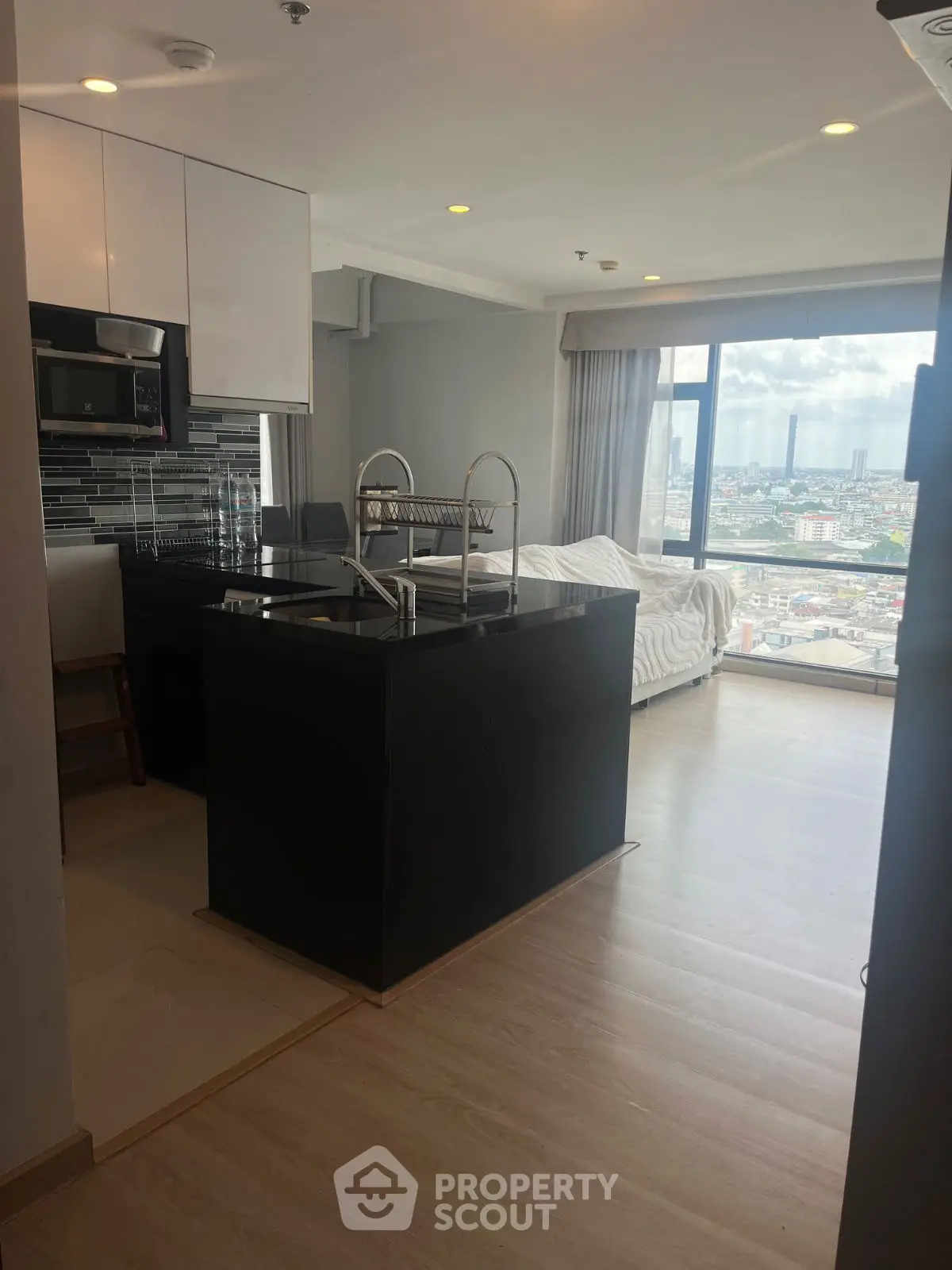 Modern open-layout kitchen with city view, featuring sleek black countertops and large windows.