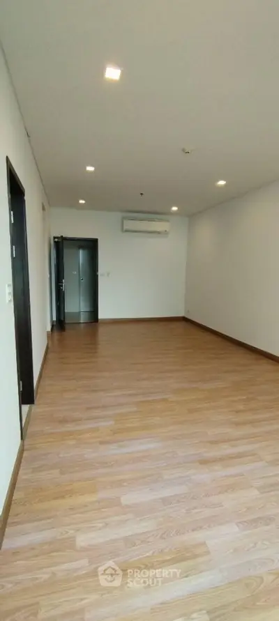 Spacious empty room with wooden flooring and air conditioning unit.