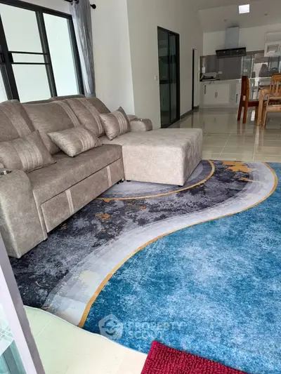 Spacious living room with modern sofa and stylish rug, open layout leading to a contemporary kitchen.
