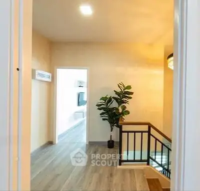 Modern hallway with wooden flooring and indoor plant, leading to a bright living area.