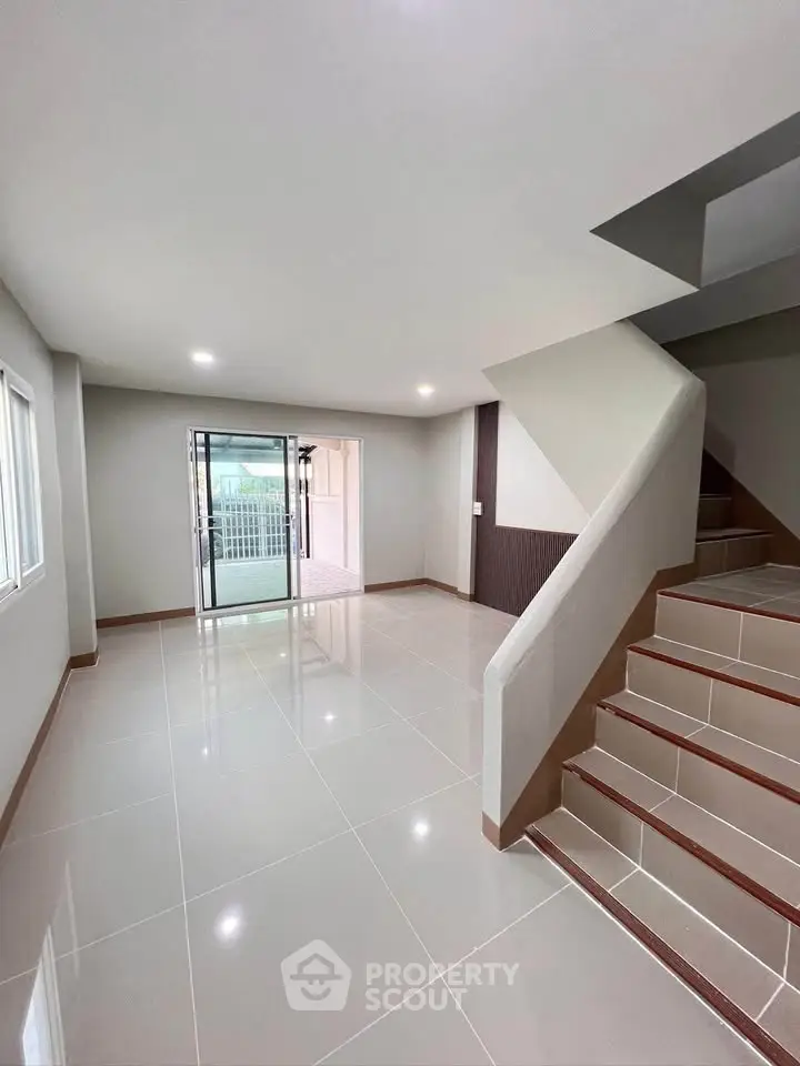 Spacious modern living room with sleek staircase and large windows, perfect for natural light.