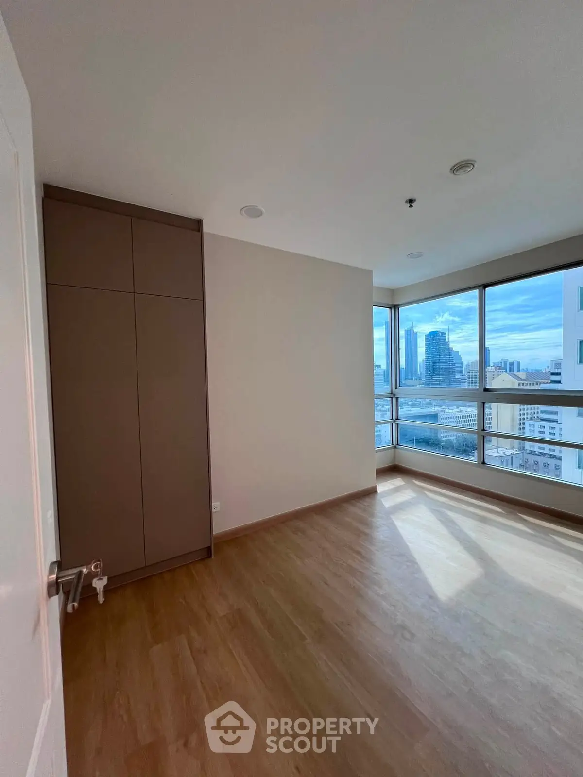 Spacious bedroom with large windows offering stunning city views and ample natural light.