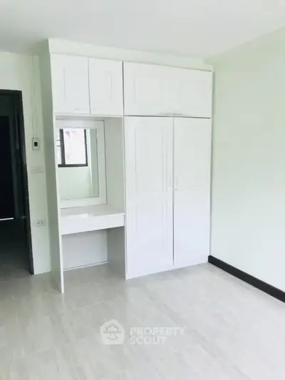 Spacious bedroom with built-in white wardrobe and vanity in modern apartment