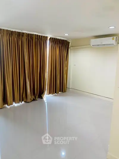 Spacious empty room with glossy tile flooring and elegant curtains, featuring air conditioning.