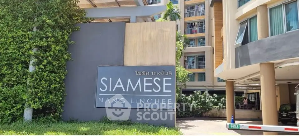 Modern condominium entrance with Siamese Nang Linchee sign and lush greenery.