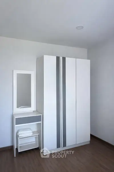 Modern minimalist bedroom with sleek wardrobe and vanity set on wooden flooring.