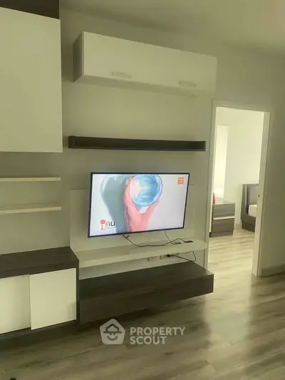 Modern living room with sleek TV unit and open doorway to bedroom, showcasing stylish interior design.