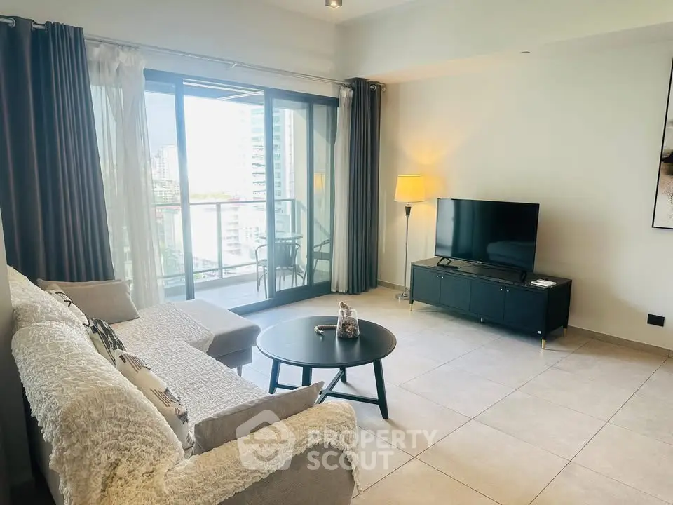Modern living room with large balcony and city view, featuring cozy sofa and flat-screen TV.