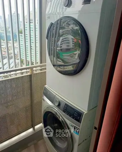 Modern stacked washing machine on a high-rise balcony with city view.