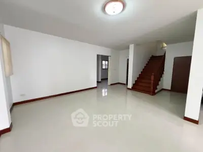 Spacious living room with polished floors and wooden staircase in modern home.