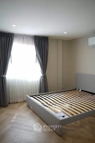 Spacious bedroom with large window and modern bed frame, perfect for relaxation.