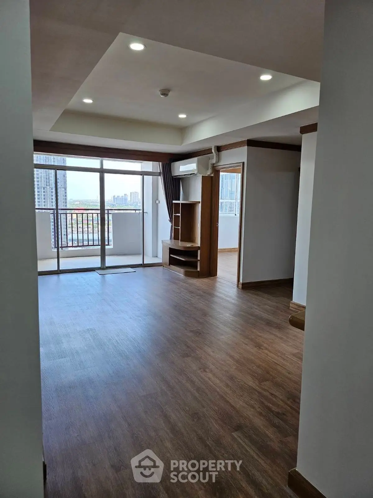 Spacious living room with wooden flooring and city view balcony in modern apartment.