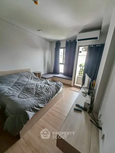 Modern bedroom with cozy bed, wooden flooring, and natural light from large window.