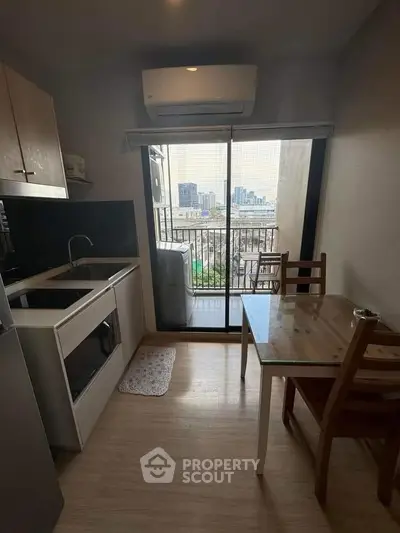 Cozy kitchen with dining area and city view from balcony, featuring modern appliances and wooden flooring.