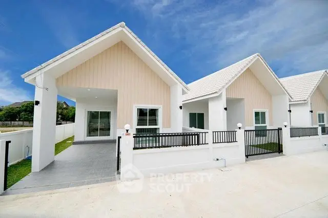 Charming modern white houses with gabled roofs and spacious front yards under a clear blue sky.