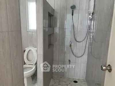 Modern bathroom with open shower and toilet, featuring sleek gray tiles.