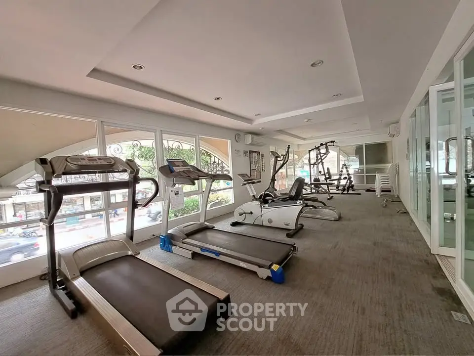 Spacious gym with modern equipment and large windows offering a vibrant city view.