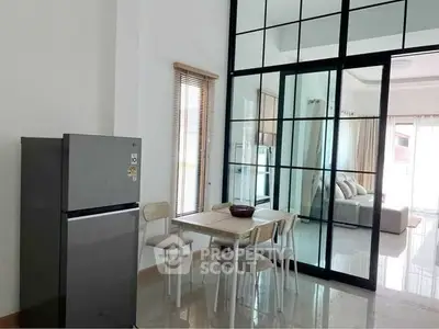 Modern dining area with glass partition and sleek refrigerator in a bright living space.