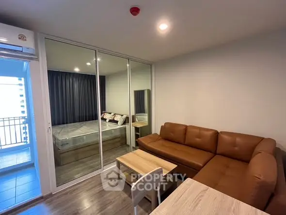 Modern living room with brown leather sofa and mirrored sliding doors leading to bedroom.