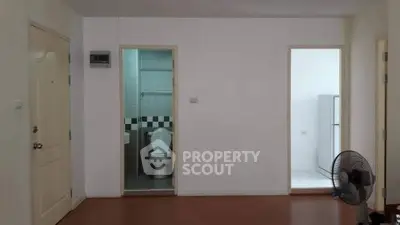 Minimalist apartment interior with bathroom and kitchen access, featuring a fan and simple decor.