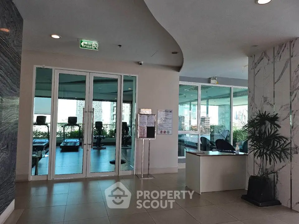 Modern gym entrance with glass doors and city view, perfect for fitness enthusiasts seeking luxury amenities.