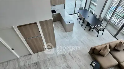 Modern open-plan living room with sleek kitchen and dining area, featuring large windows and stylish furniture.