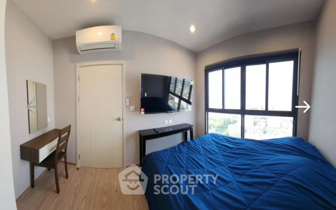 Modern bedroom with large window, blue bedding, and wall-mounted TV