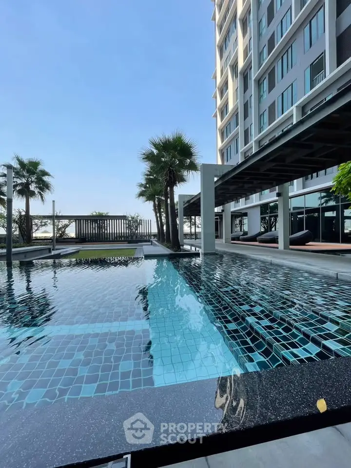 Luxurious poolside view at modern high-rise building with palm trees and clear blue sky.