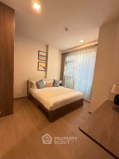 Modern bedroom with cozy bed, wooden flooring, and large window with sheer curtains.