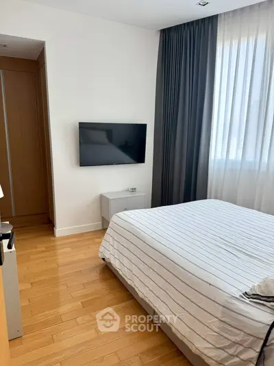 Modern bedroom with hardwood floors, wall-mounted TV, and large window with curtains.