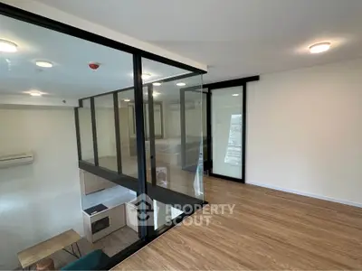 Modern loft apartment with glass partitions and wooden flooring, featuring a cozy living area and sleek design.