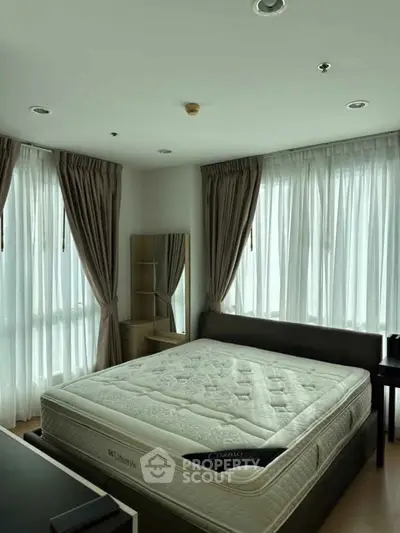 Spacious bedroom with large windows and elegant curtains, featuring a comfortable bed and stylish decor.