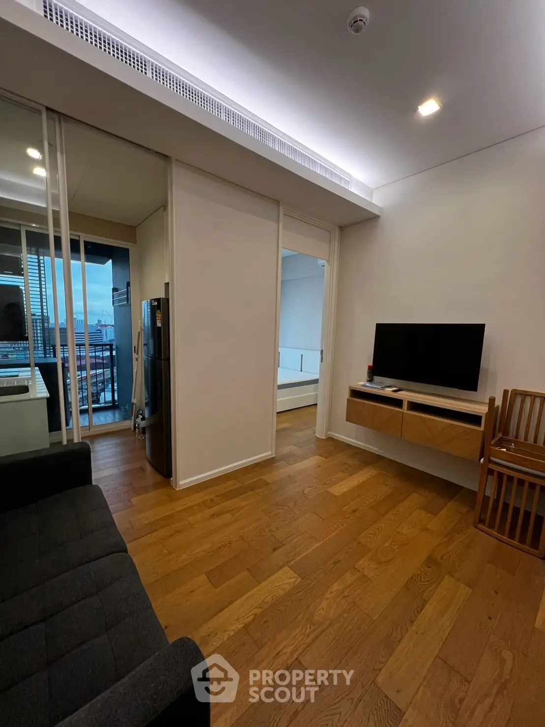 Modern living room with wooden flooring, sleek TV setup, and balcony view in a stylish apartment.
