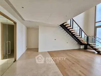 Spacious modern living room with elegant staircase and large windows offering natural light.