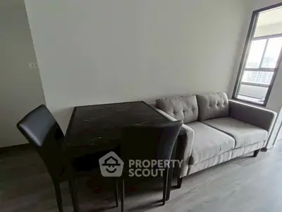 Modern living room with stylish sofa and dining table, featuring natural light from large window.