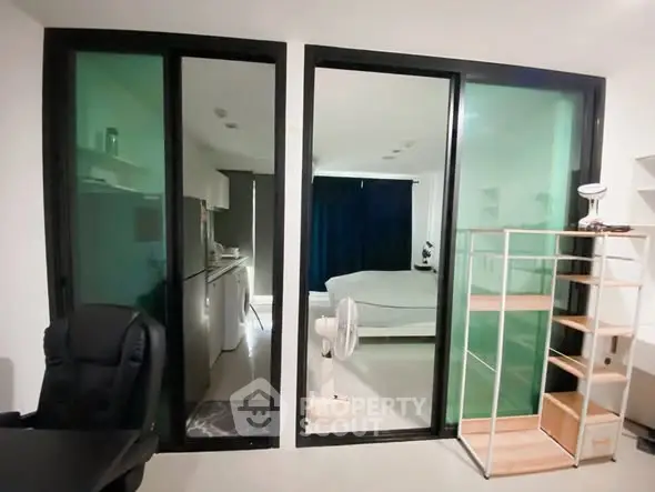 Modern apartment interior with glass partition, cozy bedroom, and compact kitchen.