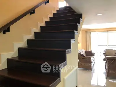 Elegant staircase leading to a cozy living area with natural light and stylish wicker furniture.