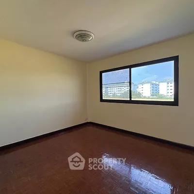Spacious empty room with large window and wooden flooring, offering potential for customization.