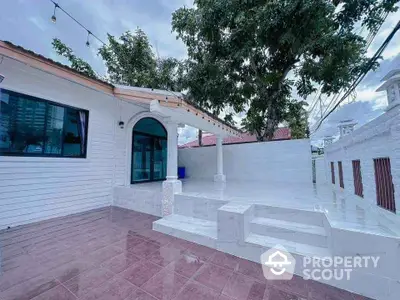 Charming white exterior home with spacious tiled patio and lush greenery.