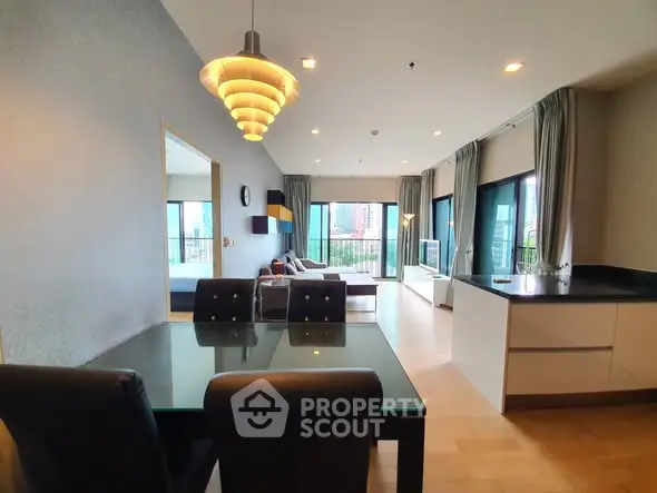 Spacious modern living room with open kitchen and city view, featuring elegant dining area and large windows.