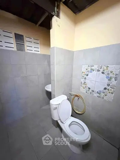 Spacious bathroom with modern toilet and tiled walls, featuring a unique decorative tile design.