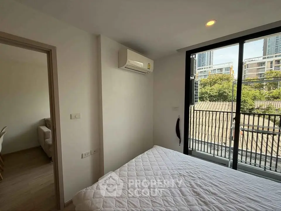 Modern bedroom with large window and city view, featuring air conditioning and minimalist decor.