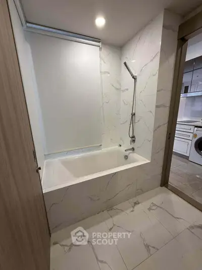 Modern bathroom with elegant marble tiles and built-in bathtub, adjacent to a laundry area with washing machine.