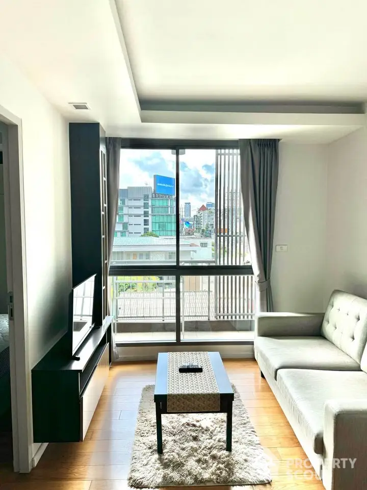 Modern living room with large window and city view, featuring sleek furniture and wooden flooring.