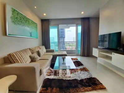 Spacious living room with modern decor and city view, featuring a comfortable sofa and large TV.