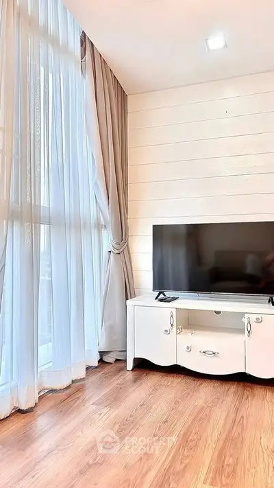Bright living room with large window, elegant curtains, and modern TV stand on wooden floor.