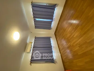 Spacious empty room with wooden flooring and large windows, perfect for customization.